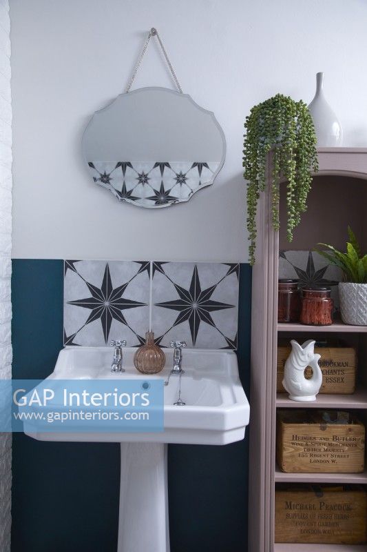 Bathroom detail showing sink, patterned tiles, vintage style mirror and open shelving storage.