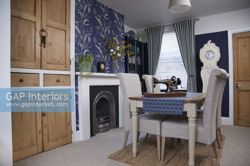 Dining room showing a fireplace, vintage wooden cupboards and blue patterned wallpaper.