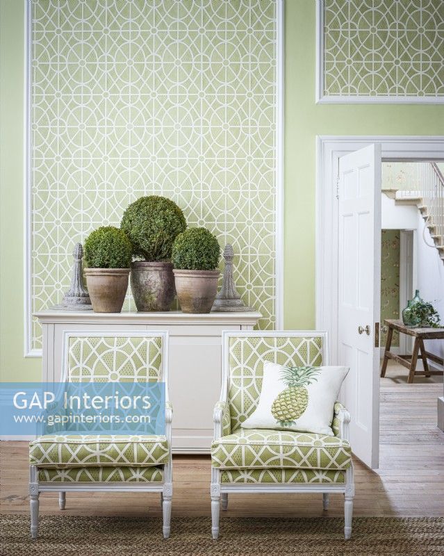 Two green patterned chairs in front of wallpapered panel wall