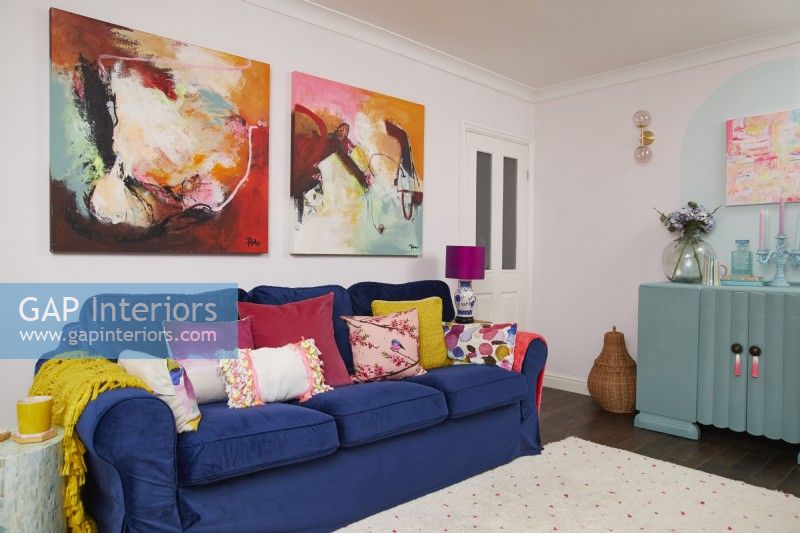 Colourful living room with a dark blue velvet sofa, large paintings and an upcycled turquoise cupboard.