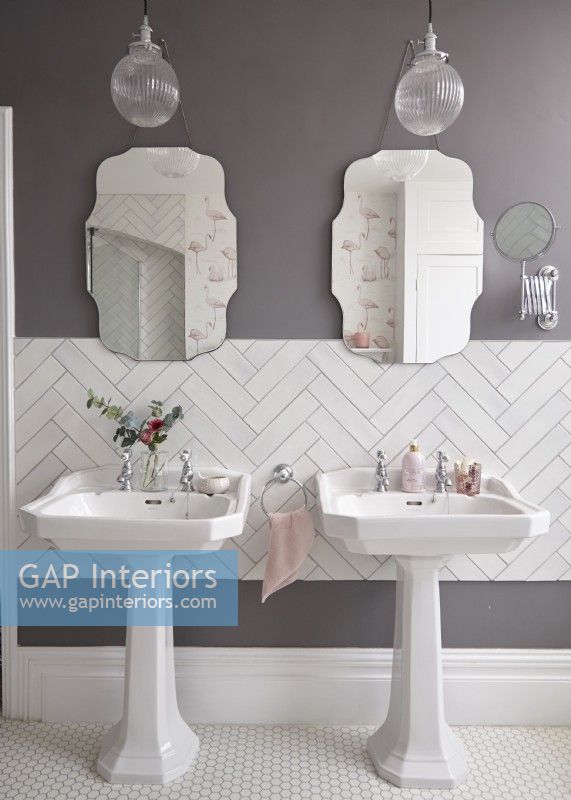 Bathroom with twin sinks, white herringbone tiling and vintage style mirrors.
