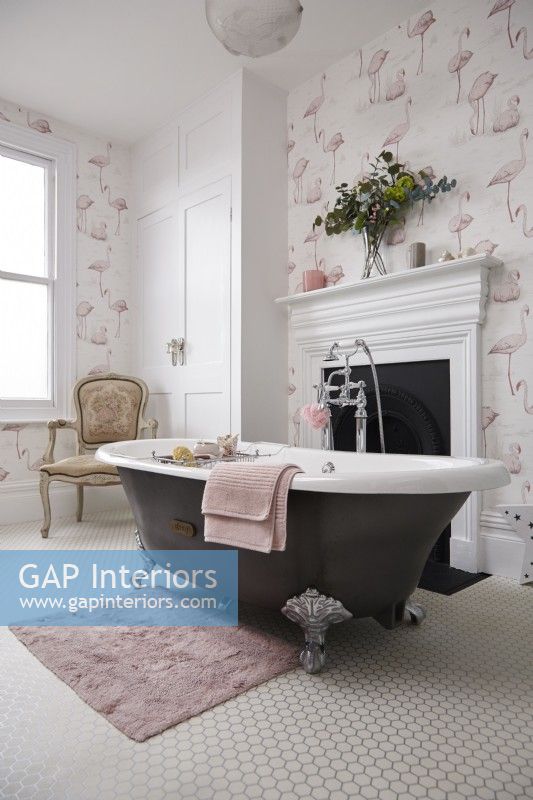 Bathroom with a rolltop bath, fireplace and flamingo wallpaper.