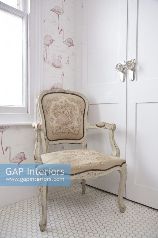 Bathroom detail showing antique chair, flamingo wallpaper and white hexagonal flooring.