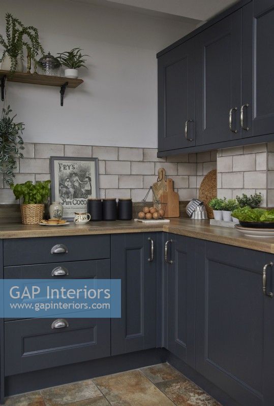 Kitchen detail showing dark grey cabinets, off white metro tiles and plants.