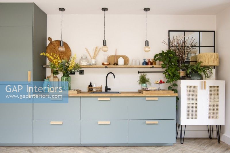 Pale green kitchen units and drawers with wood worktop and shelf