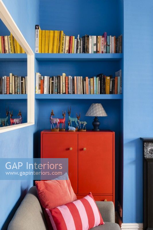 Upcycled red painted cabinet in a blue living room with book shelving above 
