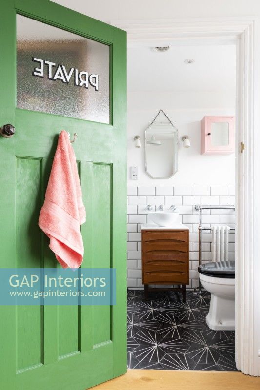 Reclaimed green door opening in to a bathroom with mid century cabinet of drawers converted to a vanity unit with sink

