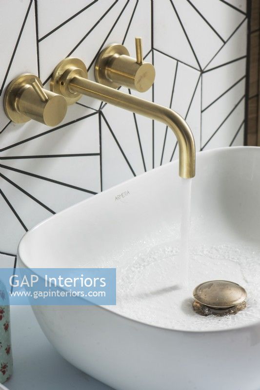 Brass tap with running water into small modern white sink