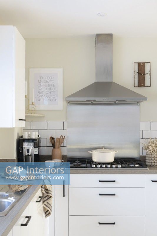 Stainless steel splashback and extractor fan behind a gas hob in a modern white kitchen