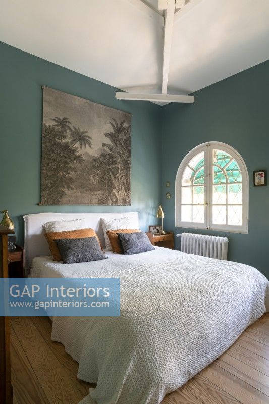 Arched window and teal blue painted walls in country bedroom