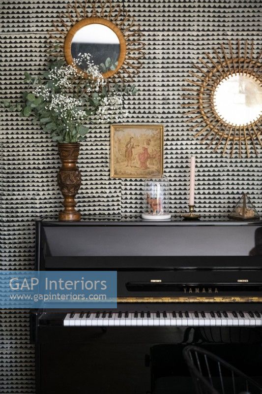 Mirrors and ornaments on patterned wall above upright piano 