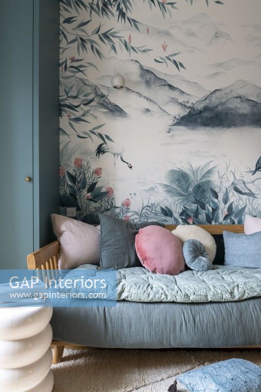 Daybed covered in pillows next to mural on bedroom wall