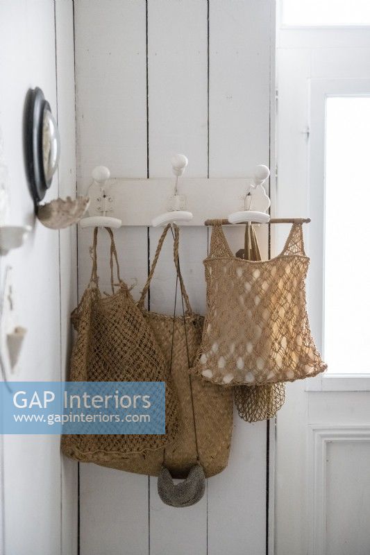 Detail of woven bags on white painted coat hooks