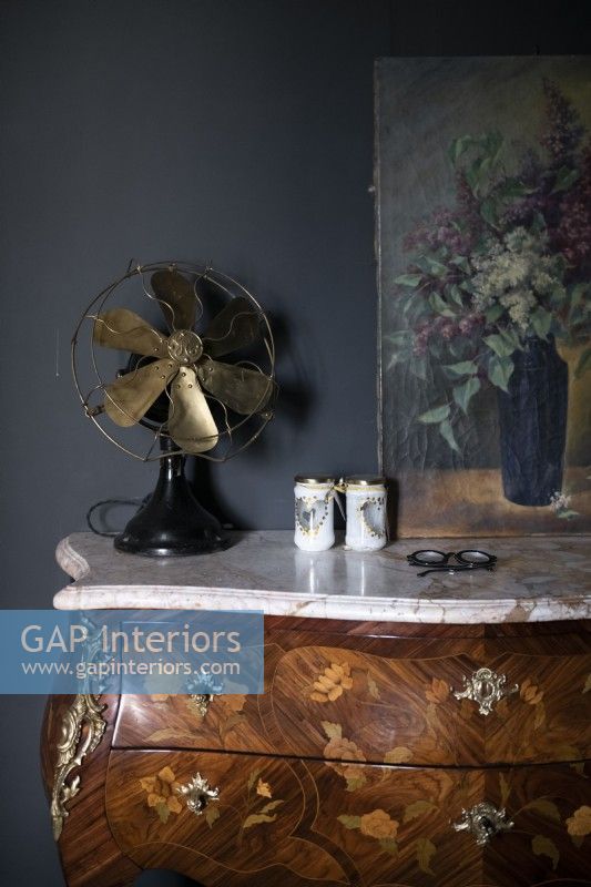Vintage fan on antique chest of drawers with painting