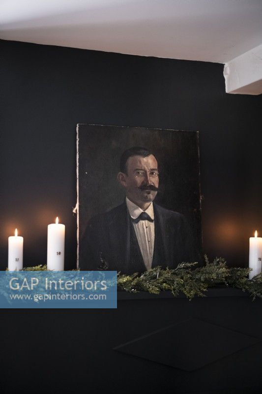 Detail of classic portrait against black wall with candles and garland