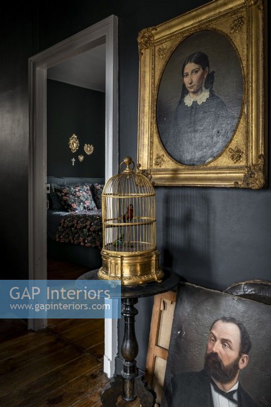 Classic portraits and golden birdcage against black painted wall