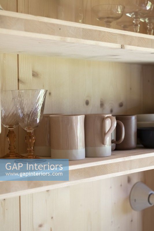 Detail of glassware and mugs on wooden kitchen shelf