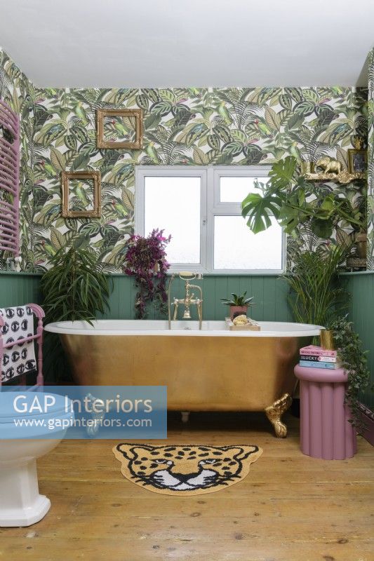 Gold bathtub in a green panelled bathroom with patterned jungle leaf wallpaper