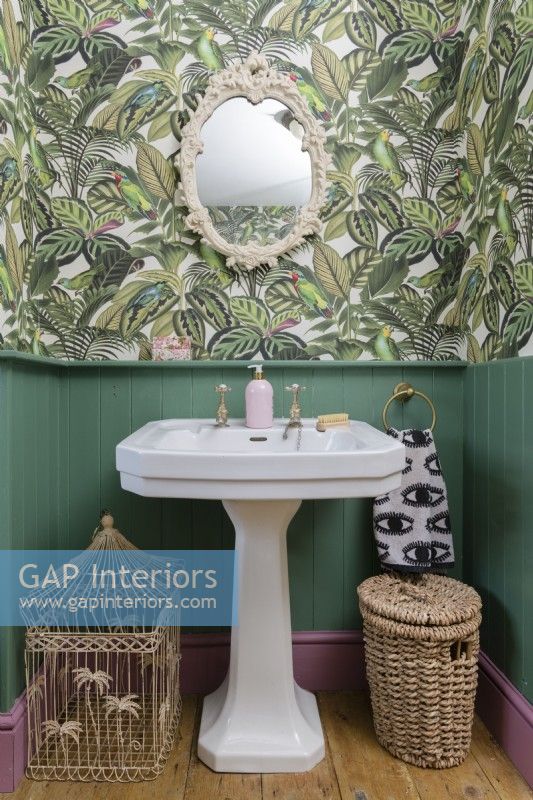 White Victorian sink in a green panelled bathroom with patterned jungle leaf wallpaper