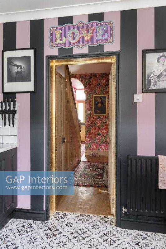 A pink and black striped kitchen wall with a view through the door to a hallway and staircase