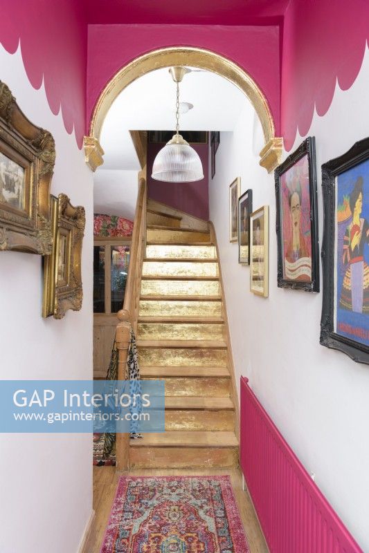 A gold painted staircase in a pink and white scalloped painted hallway