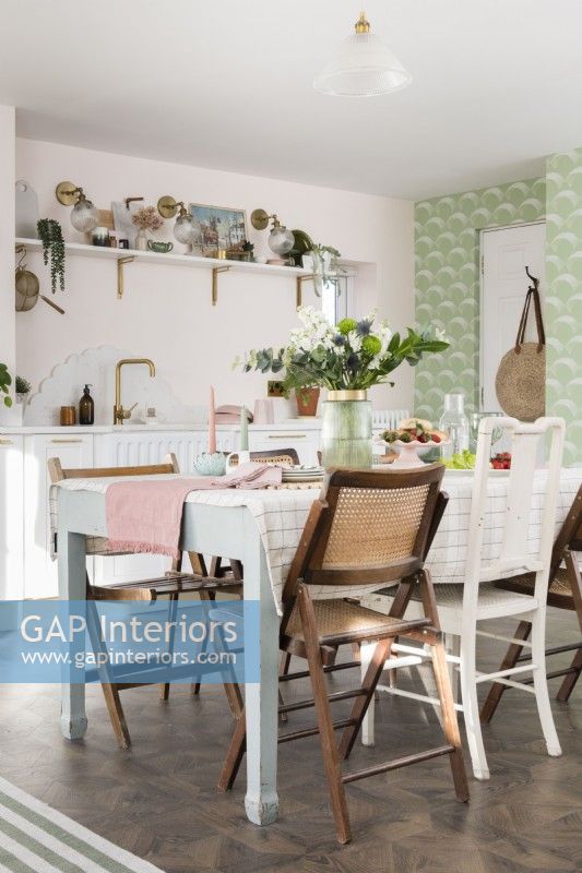 Dining table in open plan pale pink and green kitchen diner with eclectic mix of wooden chairs