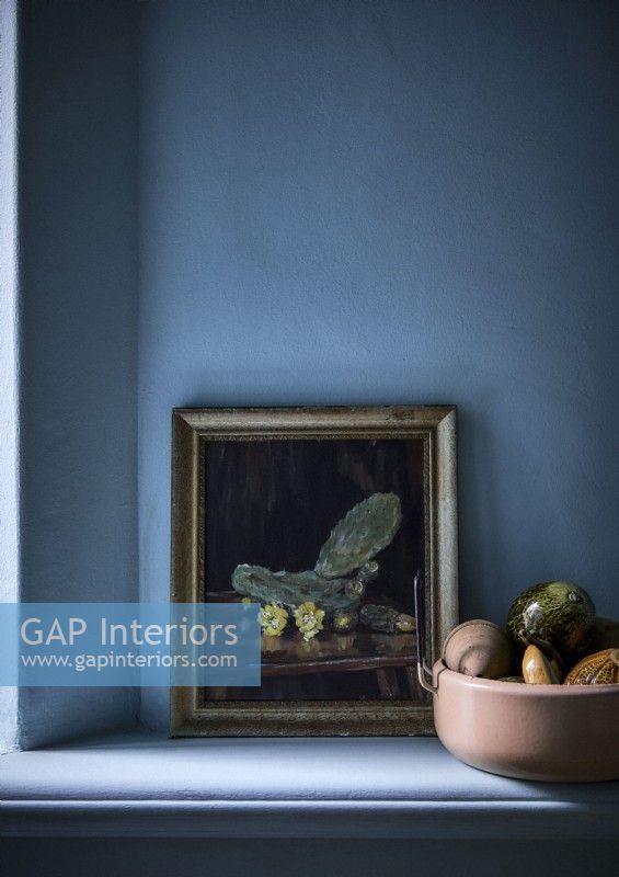 Framed still life painting and bowl of fruit on blue painted shelf