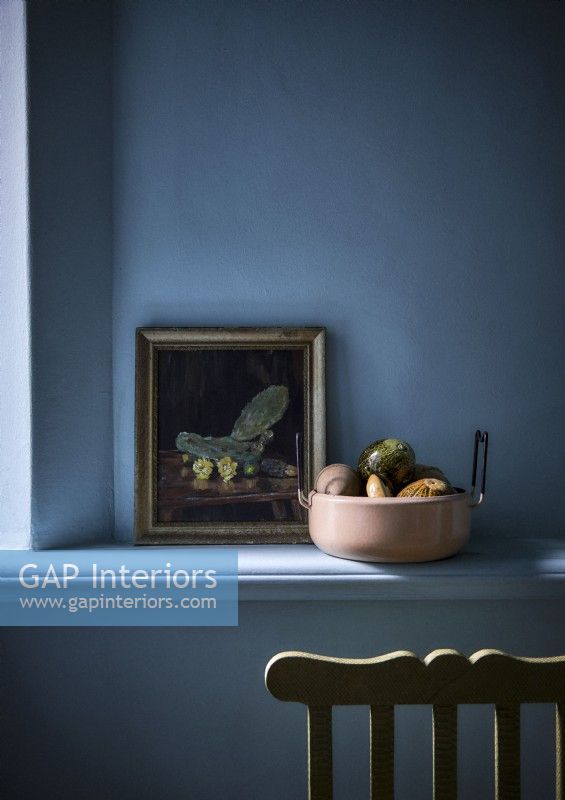 Detail of still life painting next to bowl of fruit against blue wall