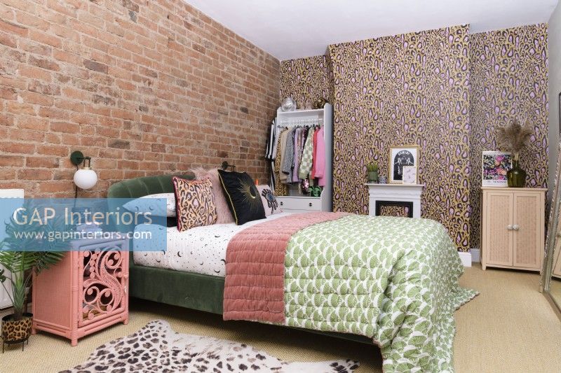 Modern bedroom in pinks and greens with a leopard print wallpapered feature wall and chimney breast and a wall with exposed brickwork 