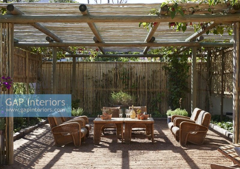 Wicker armchairs and tables under pergola on country terrace
