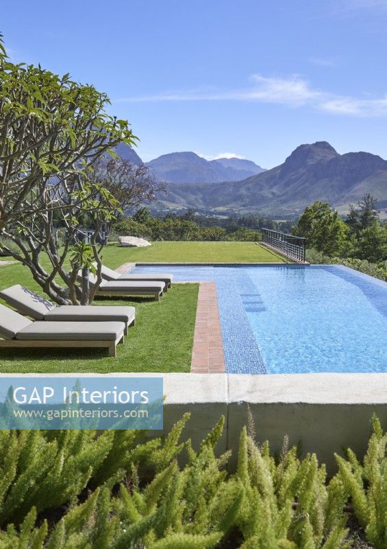 Swimming pool and gardens with loungers and mountain range beyond