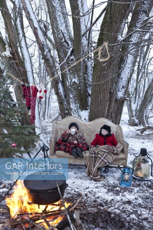 Little boy and girl on sofa  outside in the snow by campfire at Christmas