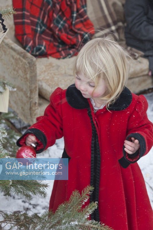 Little girls wearing red vintage coat and decorating outdoor Christmas tree in the snow