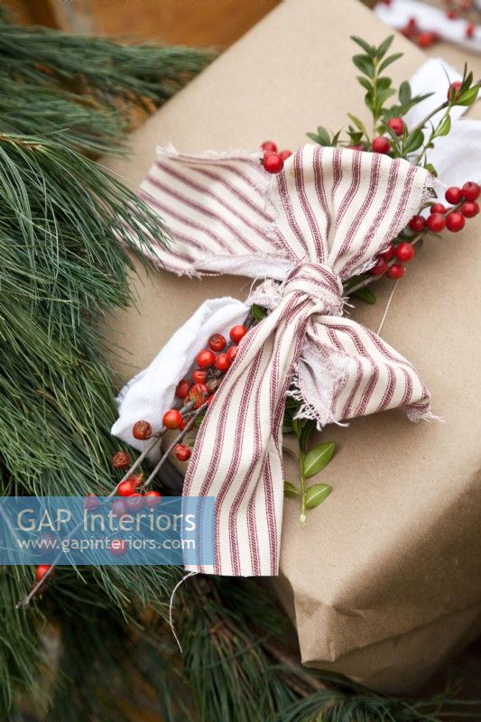Close up of Christmas gift wrapped in brown paper decorated with ribbon, greenery and berries