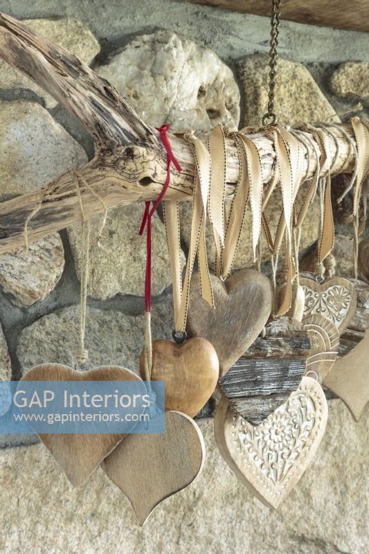 Collection of hearts from all over the world in varied materials and sizes hanging on driftwood on fireplace in living room.