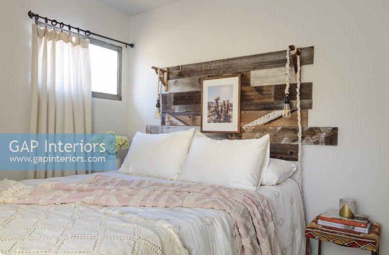 The headboard was built  using leftover scrap fence wood and made  tall enough to accommodate standing pillows and a framed picture. A small table keeps inspiring books handy for bedtime reading.