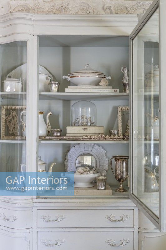 The interior of the cabinet painted in Rachelâ€™s signature palest blue grey provides just-right contrast to show-off prized possessions in a range of patinas and finishes.