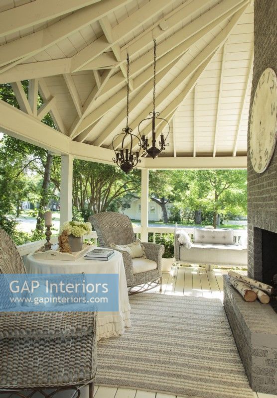 Deep overhangs give this shady porch the nostalgic feel of a classic barn. To balance the high ceilings and tall brick fireplace, Kathy chose high- backed wicker chairs that wouldnâ€™t look wimpy in the strong space. 