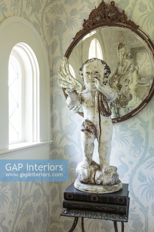 The foyer is home to an antique French cherub, a vintage mirror and metal table. The delicate blue and white wallpaper heralds the color palette of the interior of the home.