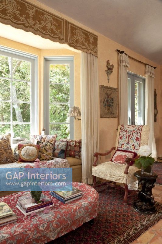 An inviting window seat and a slipcovered French chair are sited at the heart of the big hall. A parade of chic pillows presents a mini-history of textile artistry.
