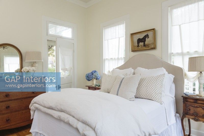 The sunny master bedroom features a new headboard upholstered in tan linen. Antiques, including an oak dresser and polished wood side tables, bring an old-world sense of coziness to the restful space.