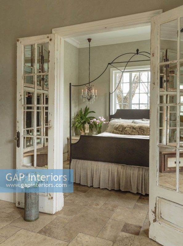  In the master bedroom, travertine floors are an eco-friendly choice that offer subtle pattern and easy care. Mirrors take the place of glass in salvaged French doors.