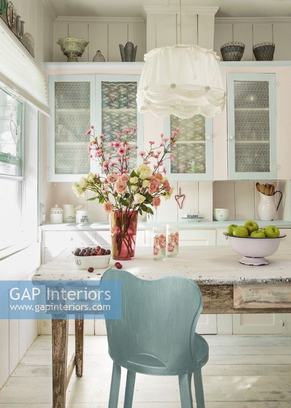 The glass doors of the original cabinets are tacked with lacy panels for a feminine look that also hides clutter. Painted a metallic blue, a kitchen chair becomes an eye-catching focal point. 