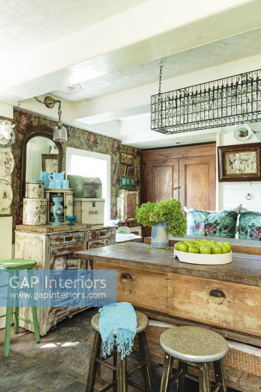 Rose patterned wallpaper, unpretentious storage cabinetry, an unusual rectangular chandelier, and a repurposed shop workbench island appear to have come together following centuries of decorating.