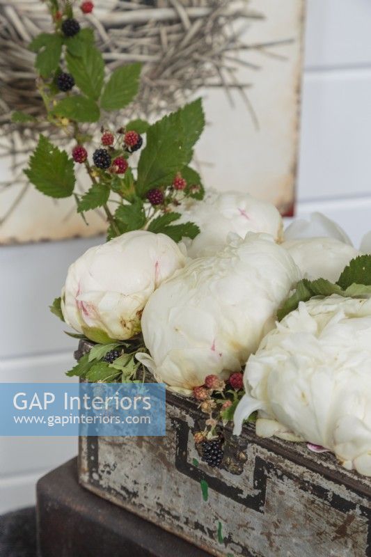 A small vintage chest function as a container for a fresh arrangement of fluffy peonies and berry-laden branches.