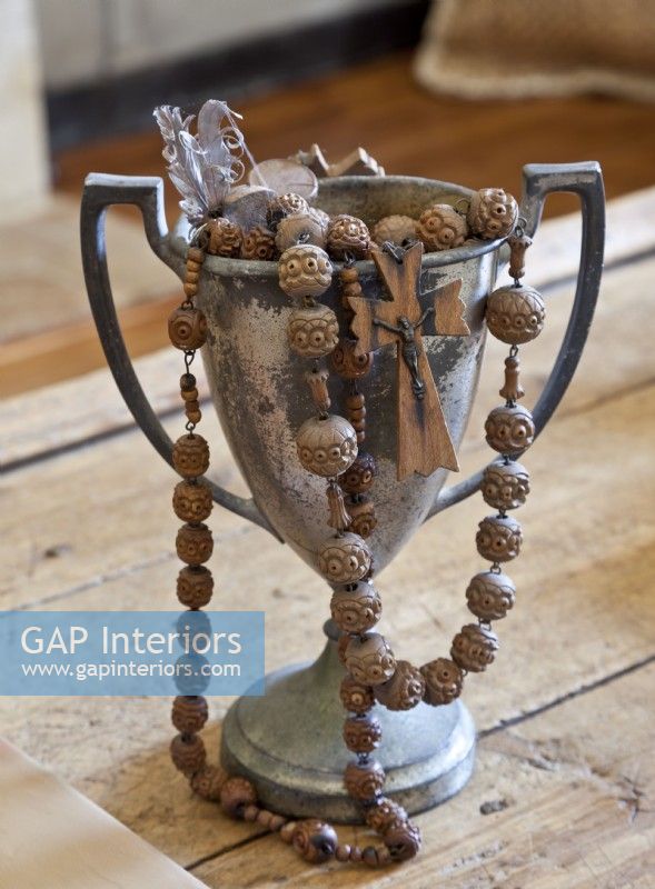 Oversize carved wooden rosary beads spill out of a tarnished loving cup. 