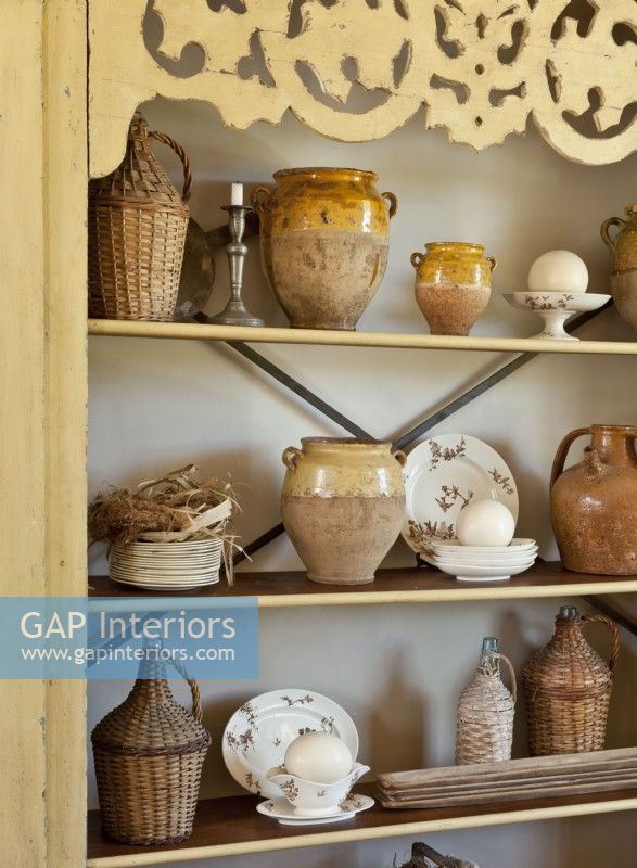 The antique cabinet holds an assortment of wicker-wrapped jugs, olive oil jars and vintage dishes.
