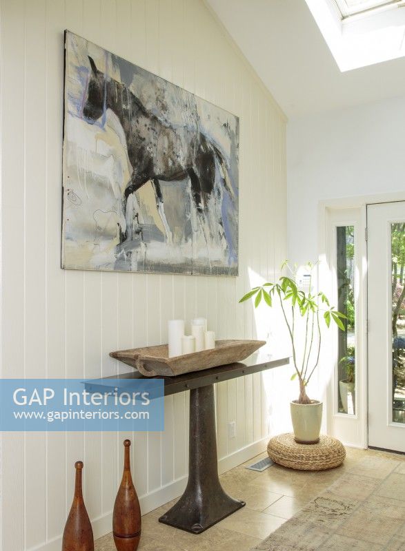 A horse portrait makes a bold statement along a simple board-and-batten wall. Beneath, a cast-iron pedestal console table anchors the vignette.