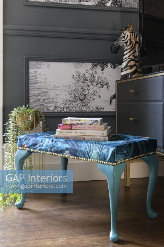 Blue patterned footstool in front of a grey paneled wall with panels filled with monochrome tropical tree wallpaper