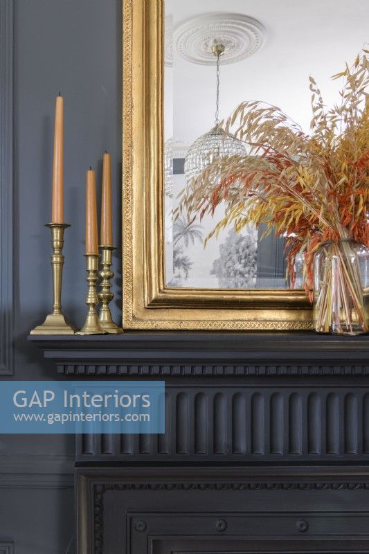 Detail of candles and candlesticks and gold framed mirror on a Victorian black painted mantlepiece